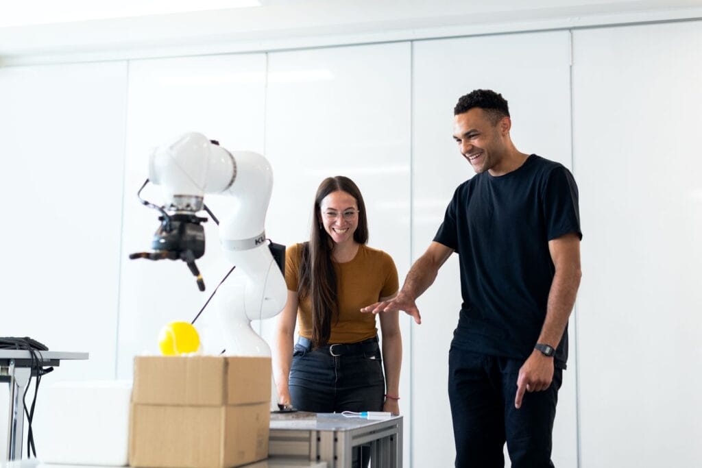 Two deep-tech founders testing a robotic arm prototype in a lab while planning grant and venture capital funding